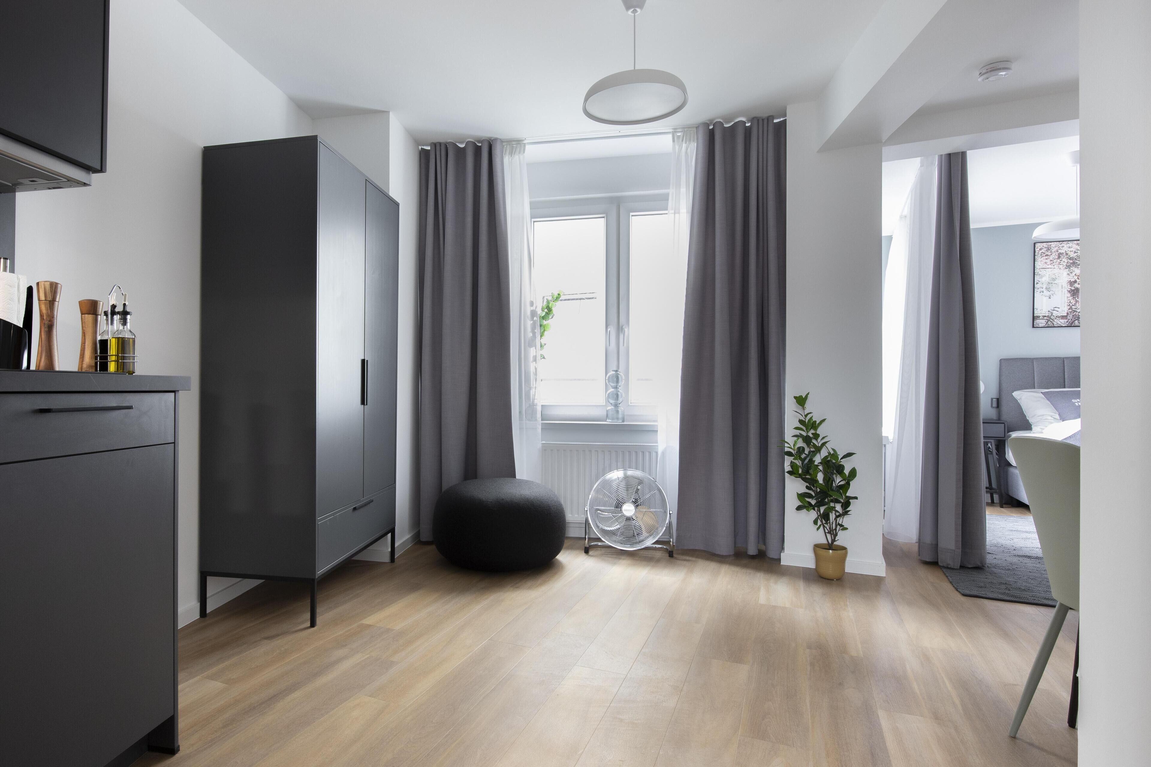 Een moderne, goed verlichte kamer met een grote kledingkast, een zwart voetenbankje, een ventilator en een potplant.