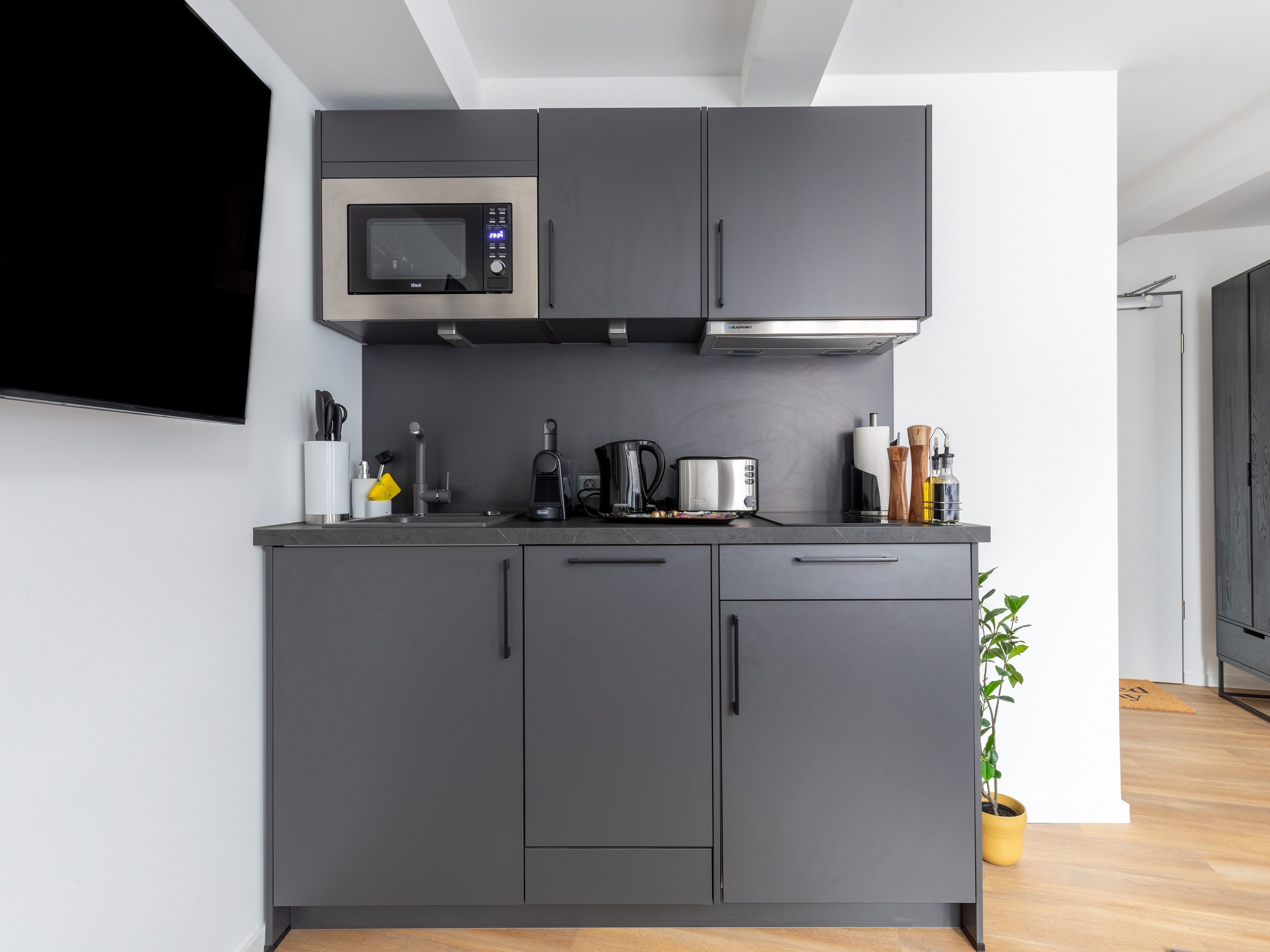 A modern kitchen with grey cabinets, a microwave, a kettle, and a coffee maker.