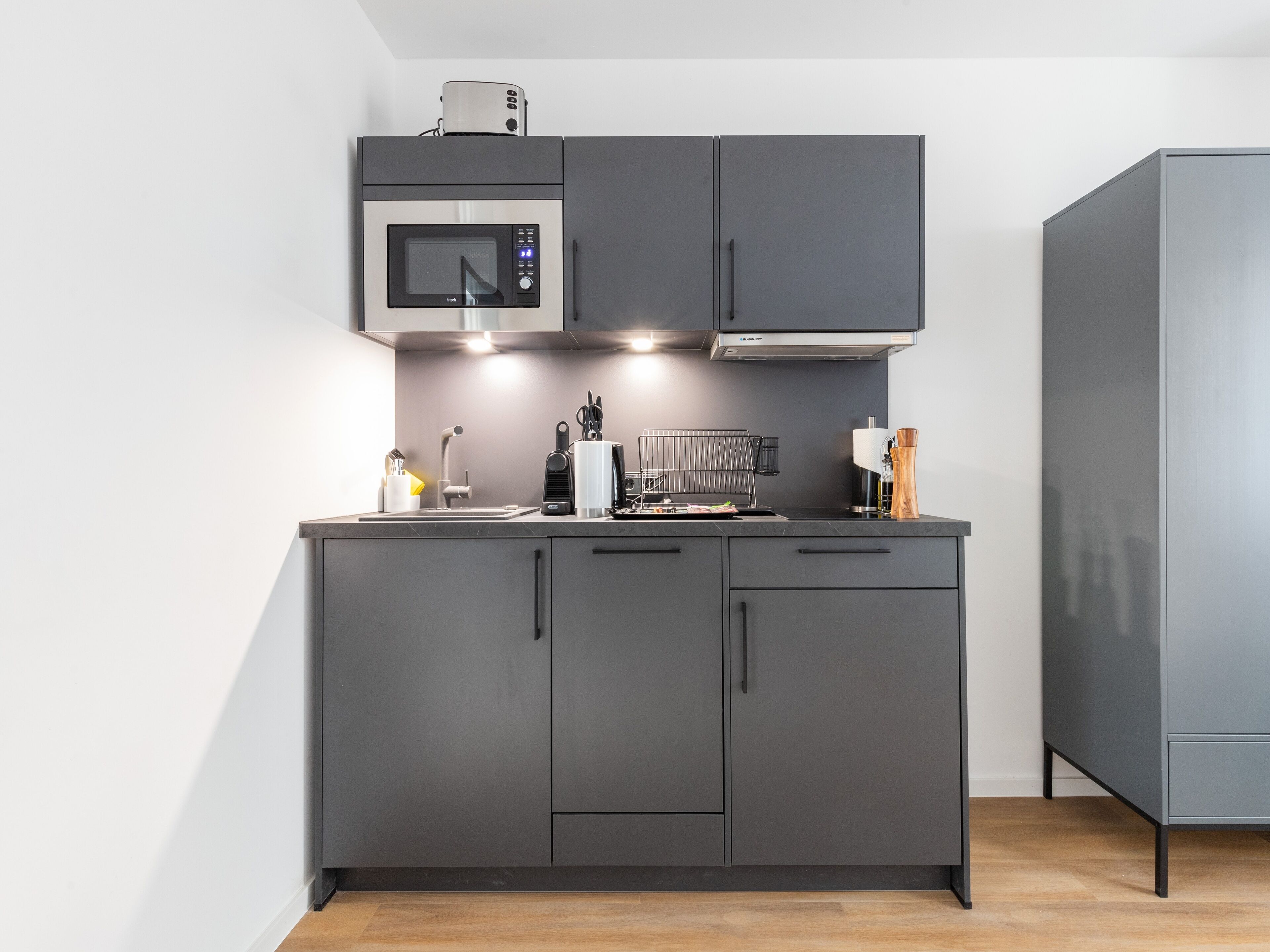 Une cuisine moderne avec des meubles de couleur grise, un four à micro-ondes encastré et une hotte aspirante.