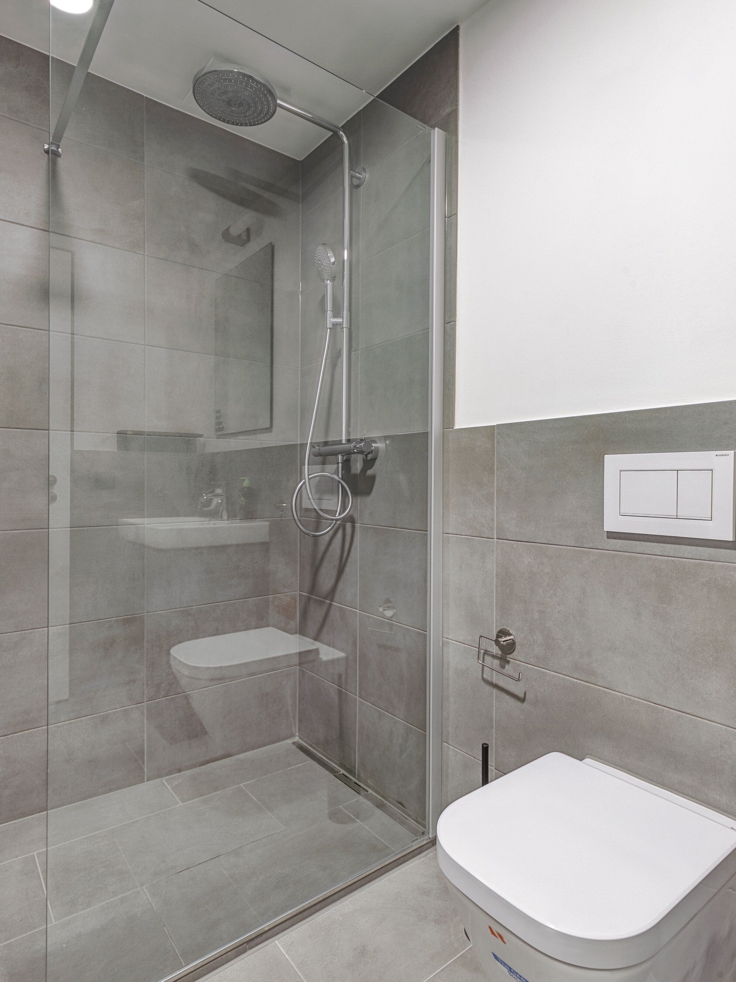 Ein modernes Badezimmer mit einer gläsernen Dusche, einer weißen Toilette und einem wandmontierten Waschbecken.