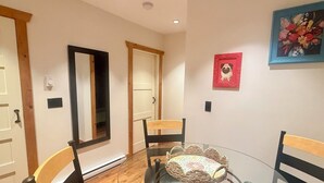 Un coin repas avec une table en verre, des chaises, un tableau accroché au mur et une porte avec un cadre en bois.