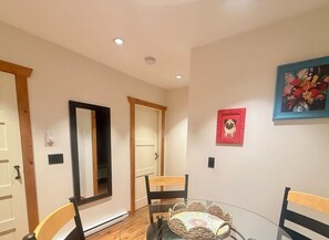 Un coin repas avec une table en verre, des chaises, un tableau accroché au mur et une porte avec un cadre en bois.