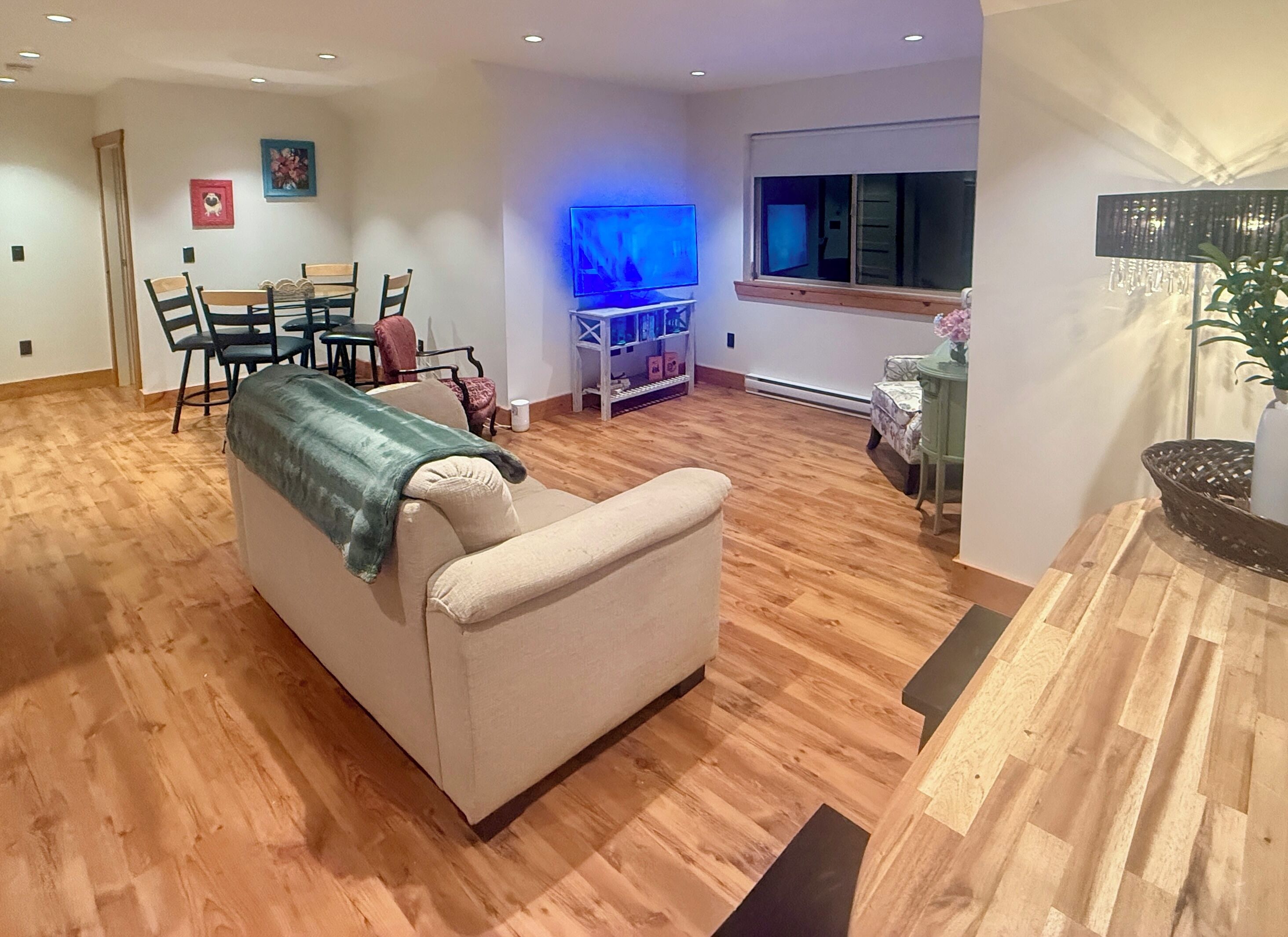 A living room with a beige sofa, wooden flooring, a TV, and a window.