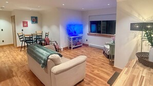 Un salon avec un canapé beige, un plancher en bois, un téléviseur et une fenêtre.