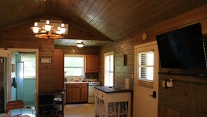 A cozy cabin-style kitchen with wooden walls, a dining area with a table and chairs, a built-in stove, and a television mounted on the wall.