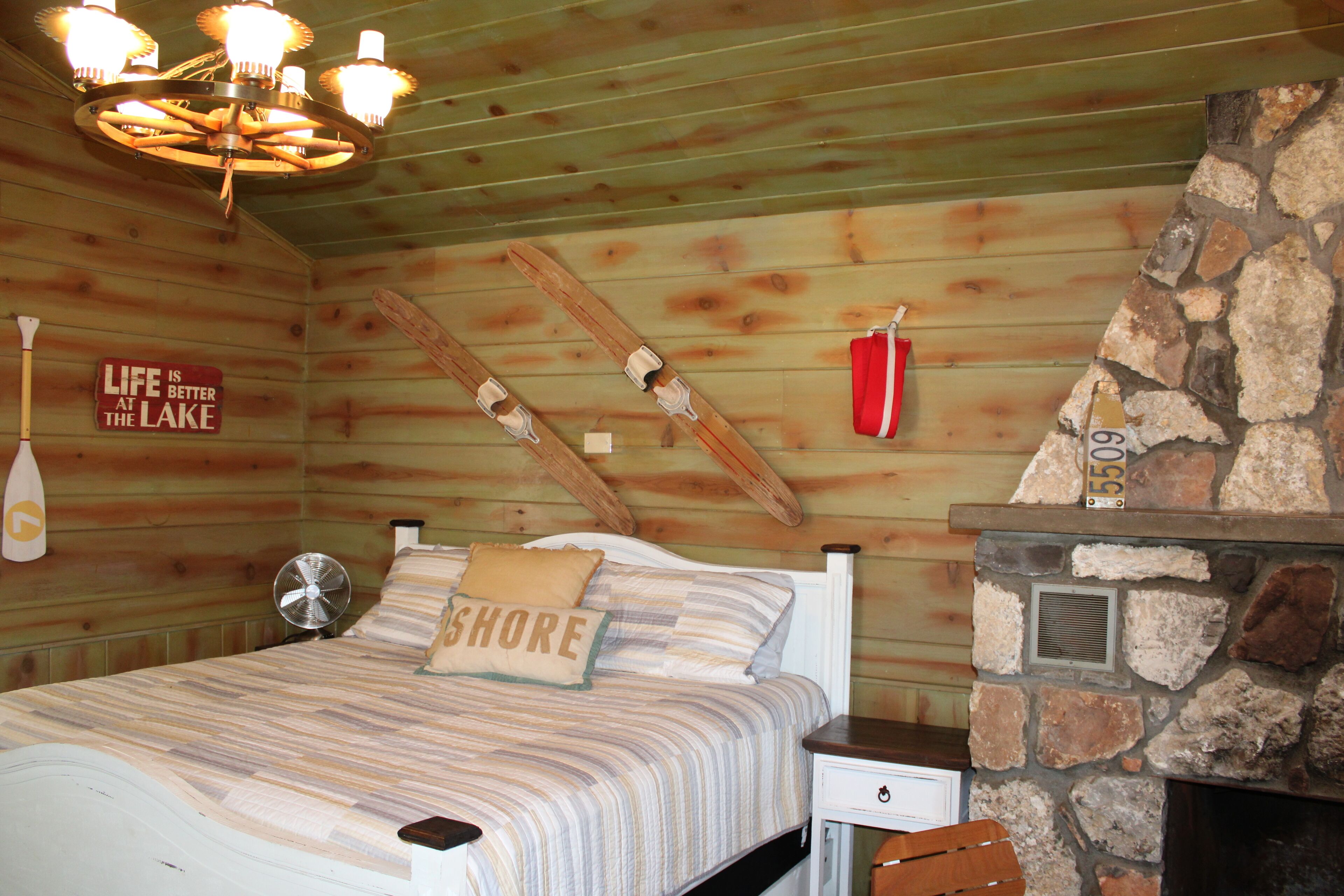 A wooden cabin bedroom with a bed, a stone fireplace, and a sign on the wall.