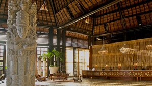 A spacious lobby with a high ceiling, a large stone column, potted plants, and a reception desk with hanging lamps. - 5 star resort week of mexico open held at same resort (Nayarit CP)