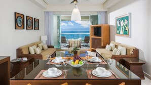 A dining area with a glass table, chairs, and a fruit bowl. There are sofas and a television on the right. The room has a view of the ocean. - 5 star resort week of mexico open held at same resort (Nayarit CP)