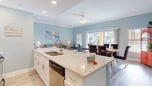 A modern kitchen with a central island, a dining area with a table and chairs, and a view of the outdoors through large windows.