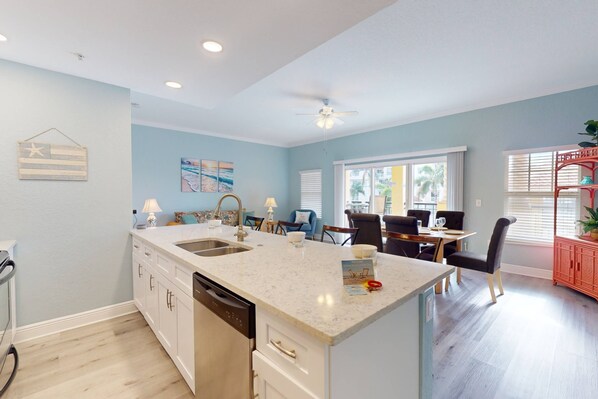 A modern kitchen with a central island, a dining area with a table and chairs, and a view of the outdoors through large windows.