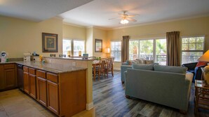 A spacious living area with a kitchen, dining table, and a large window providing a view of the outdoors. - Two Private Balconies! Heated Waterfront Pool & Hot Tub, Fish From the Dock, Just Steps to the Beach (Treasure Island)