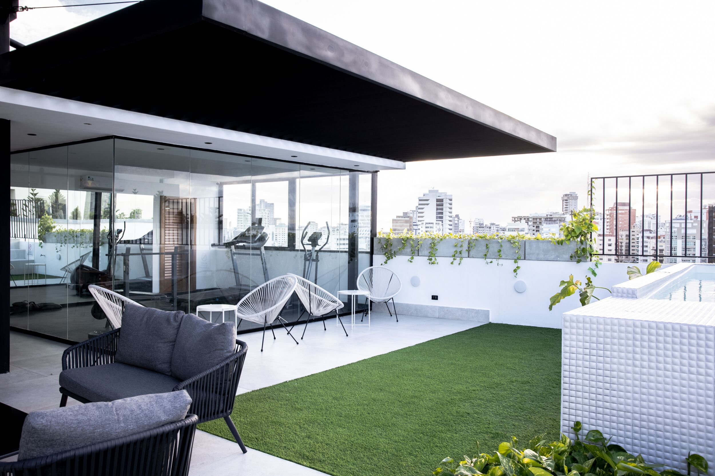 A modern rooftop terrace with glass walls, outdoor seating, and a view of the city skyline.