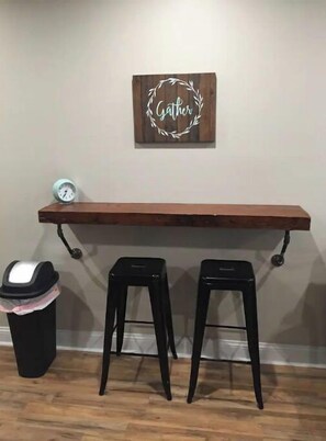 A cozy space with a bench and stools, featuring a wall-mounted clock and trash bin.