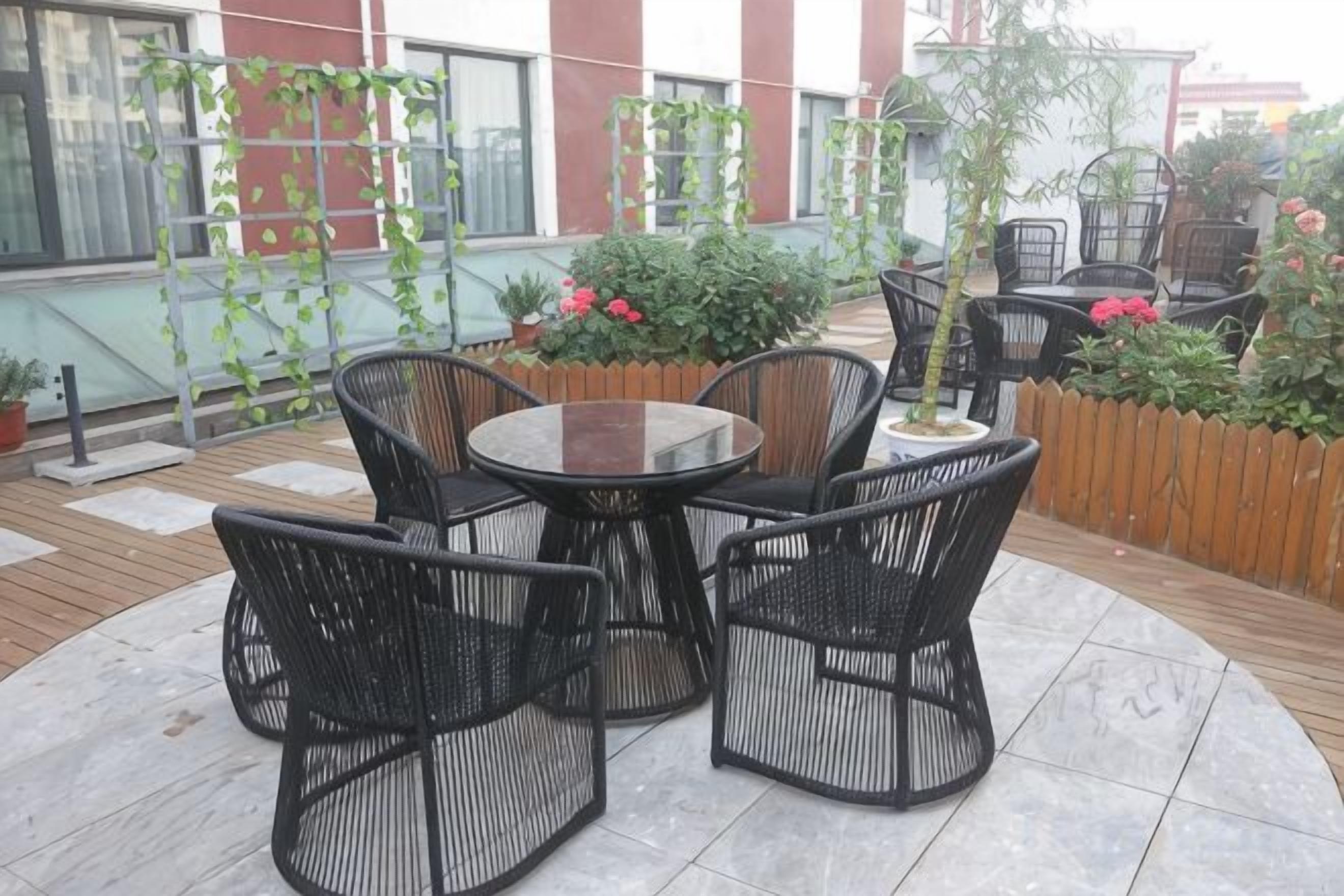 An outdoor patio with a round table and four chairs, surrounded by potted plants and a wooden fence.