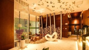 Un moderno vestíbulo de hotel con piso de mármol, una gran escultura abstracta blanca y una partición de vidrio con un diseño geométrico.
