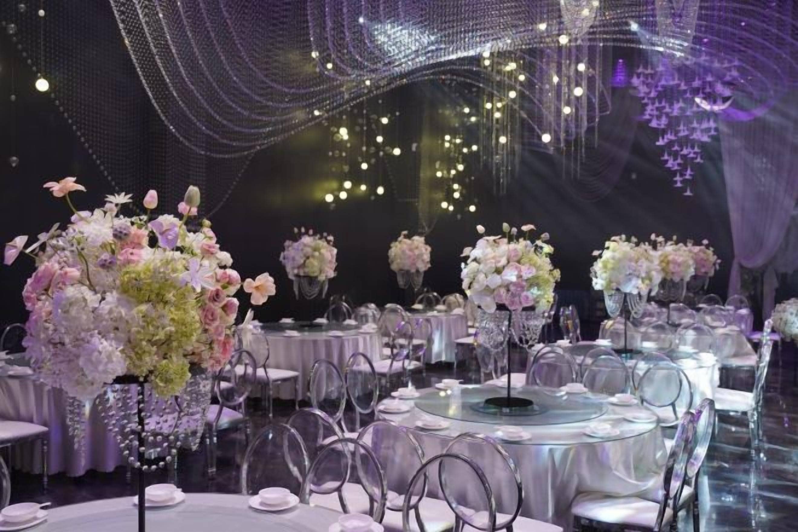 A banquet hall with round tables, chairs, and floral centerpieces.