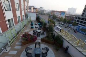 A rooftop terrace with outdoor seating, a view of the city, and a street below.
