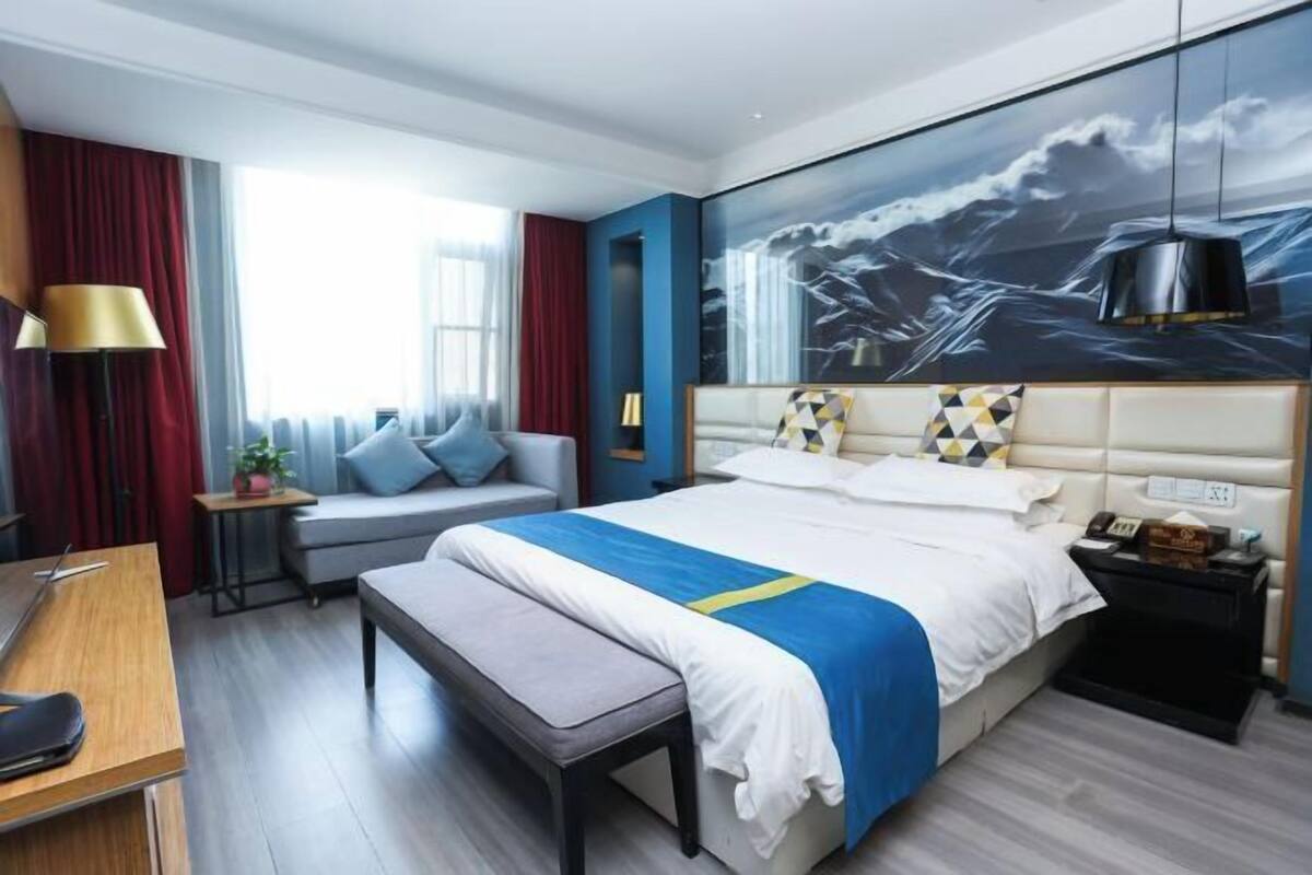 Quarto de hotel moderno com uma cama grande, uma escrivaninha, um banco e um sofá.