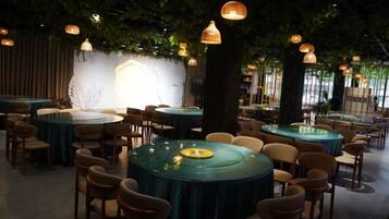 A restaurant with round tables and chairs, a wall with a light feature, and hanging lights.
