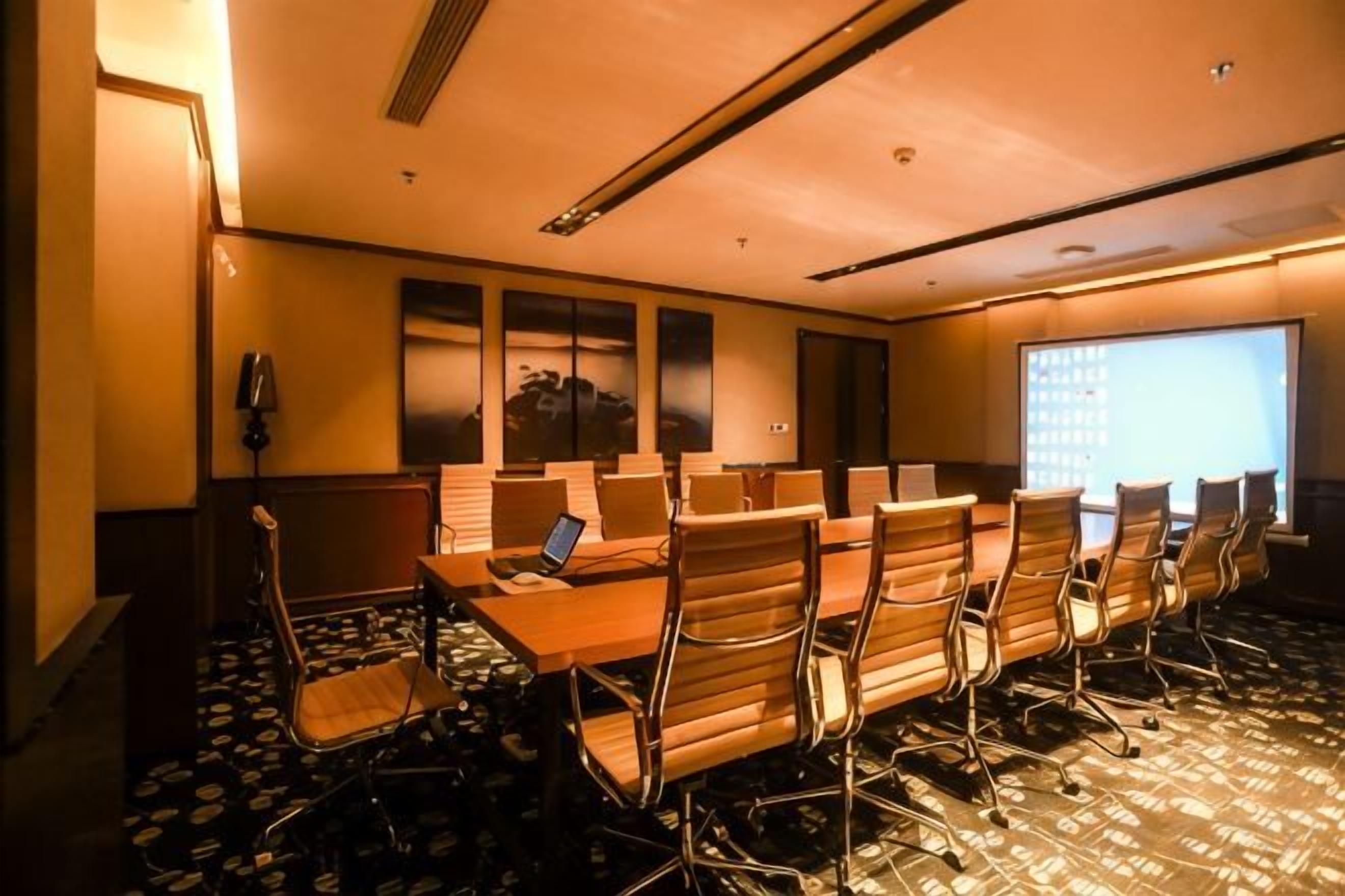 A conference room with a long table, chairs, a projector screen, and a carpeted floor.