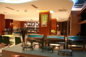A hotel lobby with seating areas, a reception desk, and a wall with a poster.