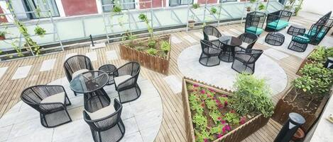 Una terraza en la azotea con mobiliario exterior, macetas y vistas de la fachada del edificio.