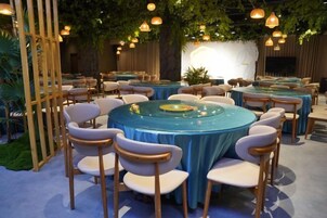 Un salón de conferencias con mesas y sillas redondas, un escenario con fondo y luces colgantes.