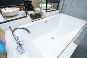 A modern bathroom with a large white bathtub, a chrome faucet, and a small wooden tray with toiletries. - Ceeci Hotel (Xichuan)