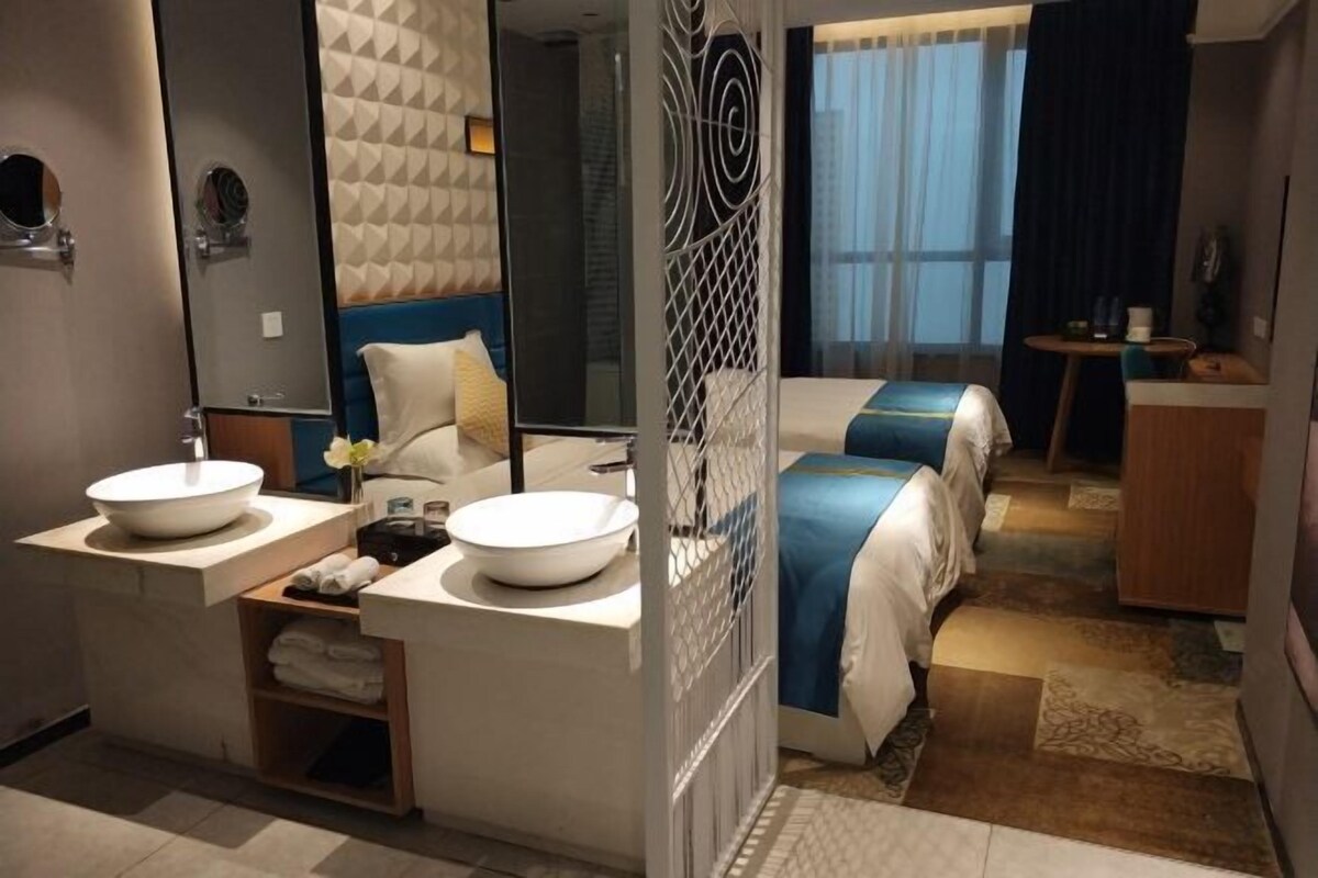 A modern hotel room with two beds, a large mirror, a round sink, and a small table.