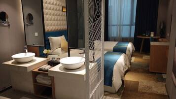 A modern hotel room with two beds, a large mirror, a round sink, and a small table.