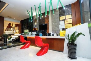 A hotel reception area with a counter, red chairs, a potted plant, and a modern ceiling design. - Ceeci Hotel (Xichuan)
