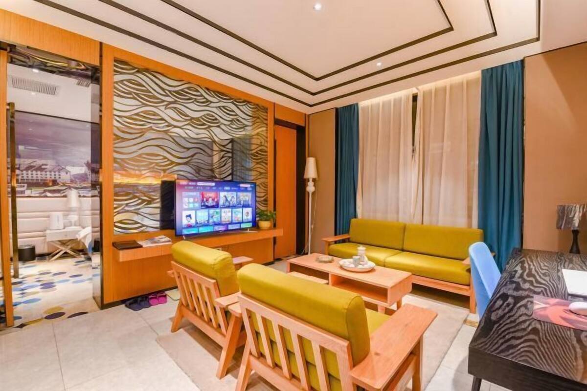 Quarto de hotel moderno com sofá, televisão, mesa de jantar e parede estampada.