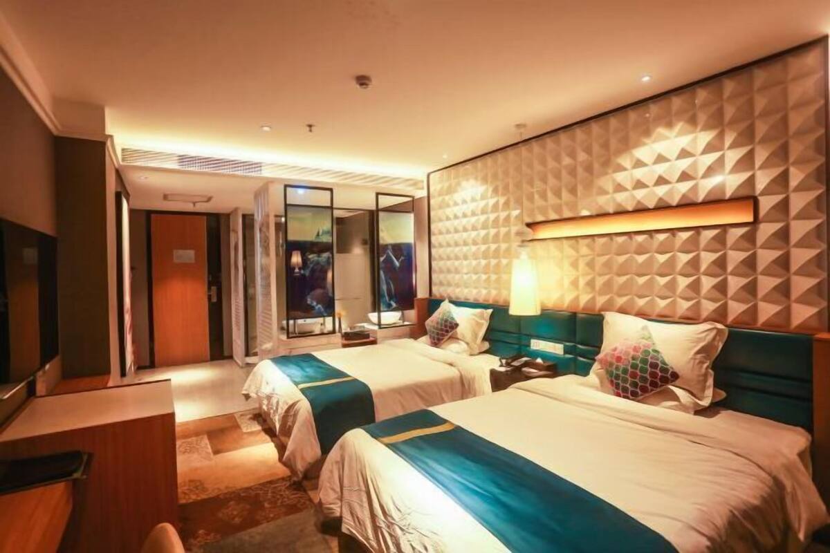 Quarto de hotel com duas camas, uma escrivaninha, televisão e uma janela grande.