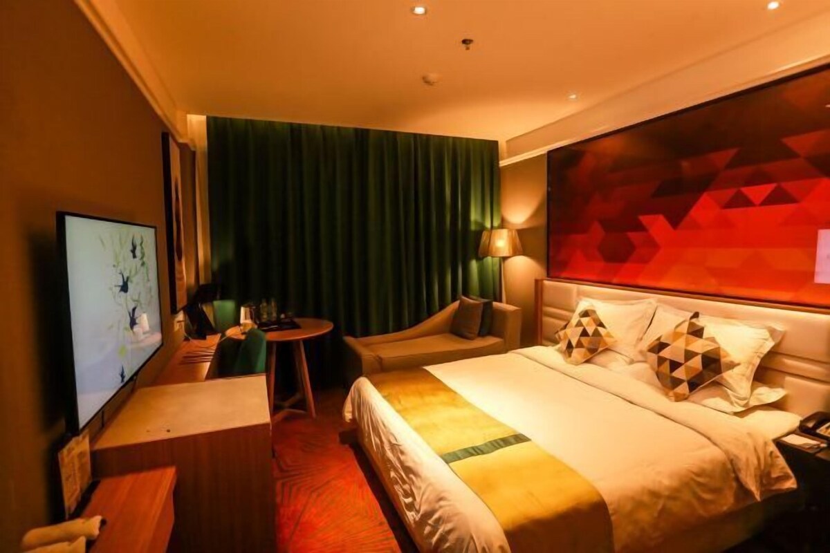 A hotel room with a bed, a desk, a chair, a TV, and a green curtain.