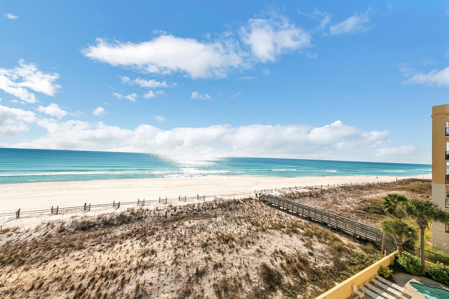 Une vue sur la plage, avec un sentier de sable menant à un bâtiment doté d’une piscine.