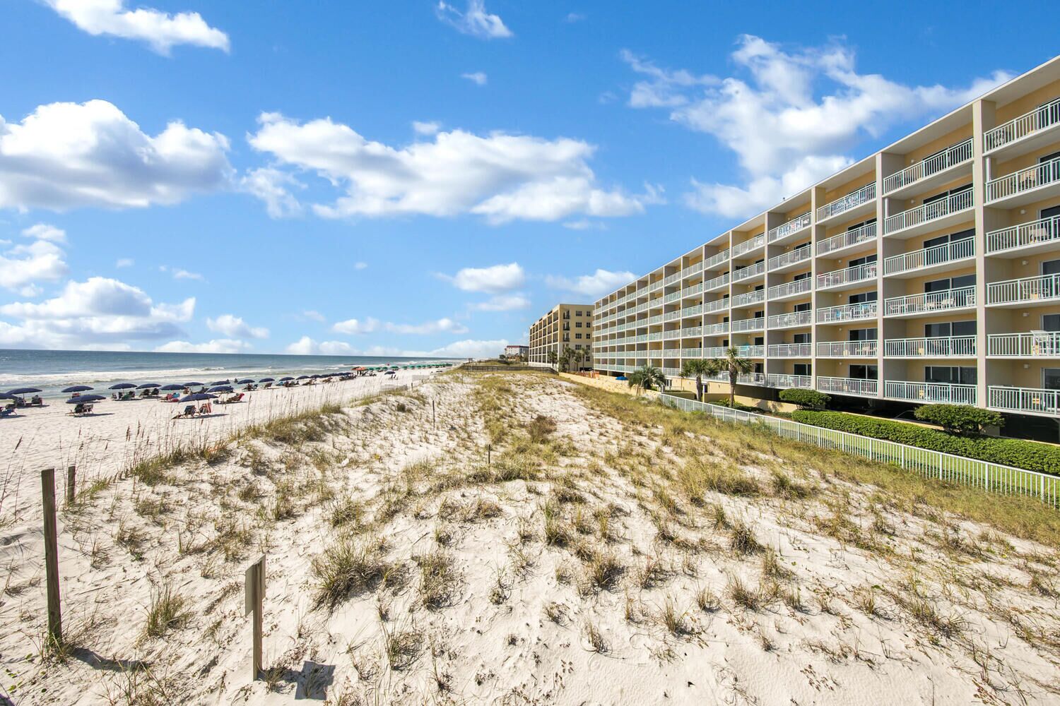 Un hotel sulla spiaggia con numerosi balconi, una spiaggia sabbiosa e un cielo sereno.
