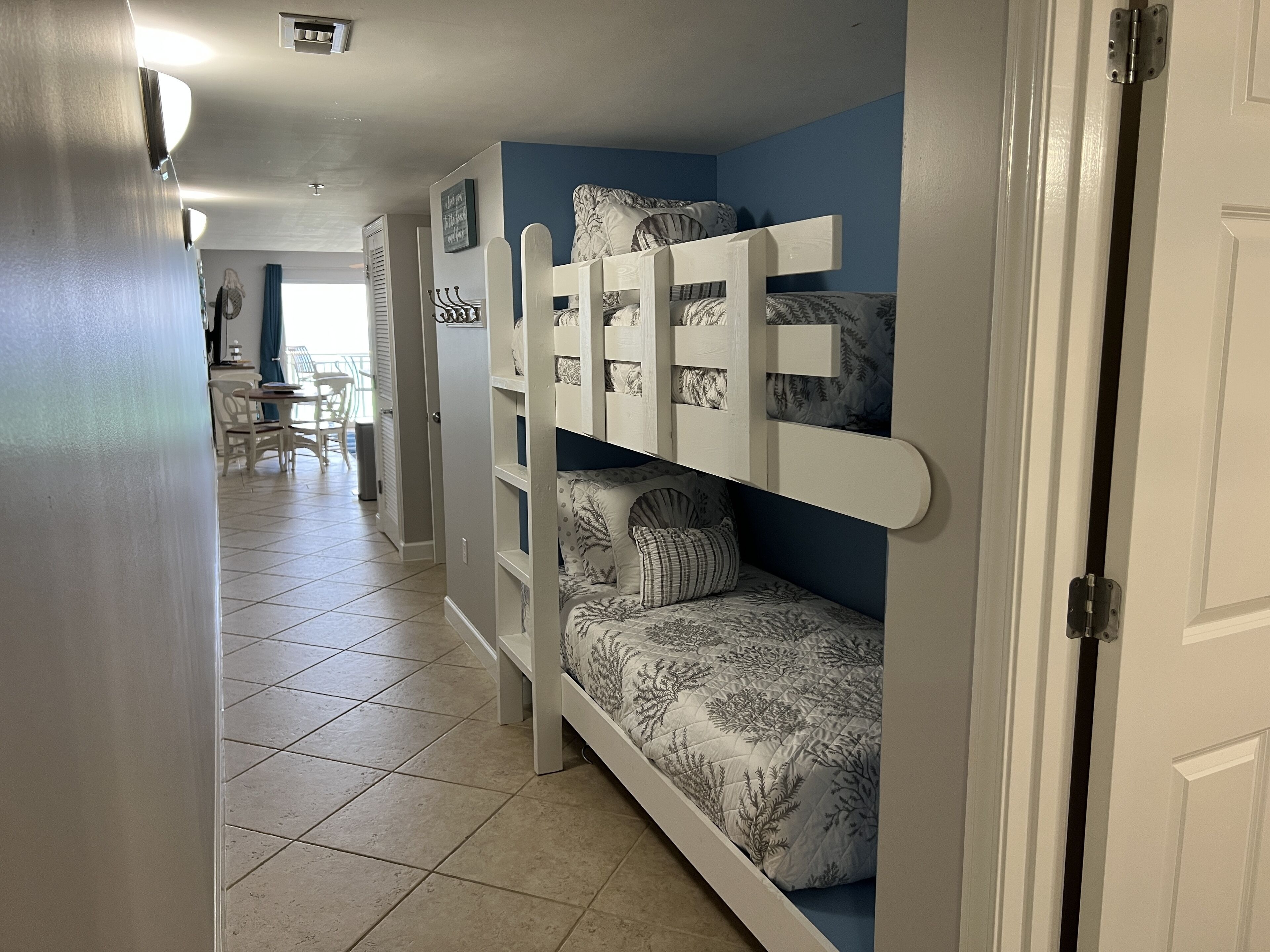 A bunk bed with a patterned bedspread, a white door frame, and a tiled floor.