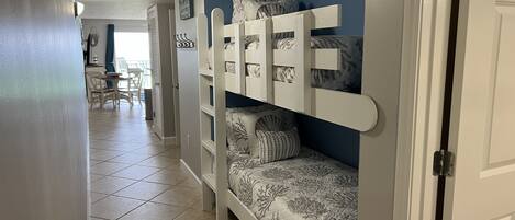 A bunk bed with a patterned bedspread, a white door frame, and a tiled floor.