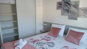 A neatly made bed with a floral bedspread, two pillows, and rolled towels on a pink blanket.