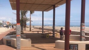 A covered outdoor area with a wooden floor, benches, and a view of the beach.