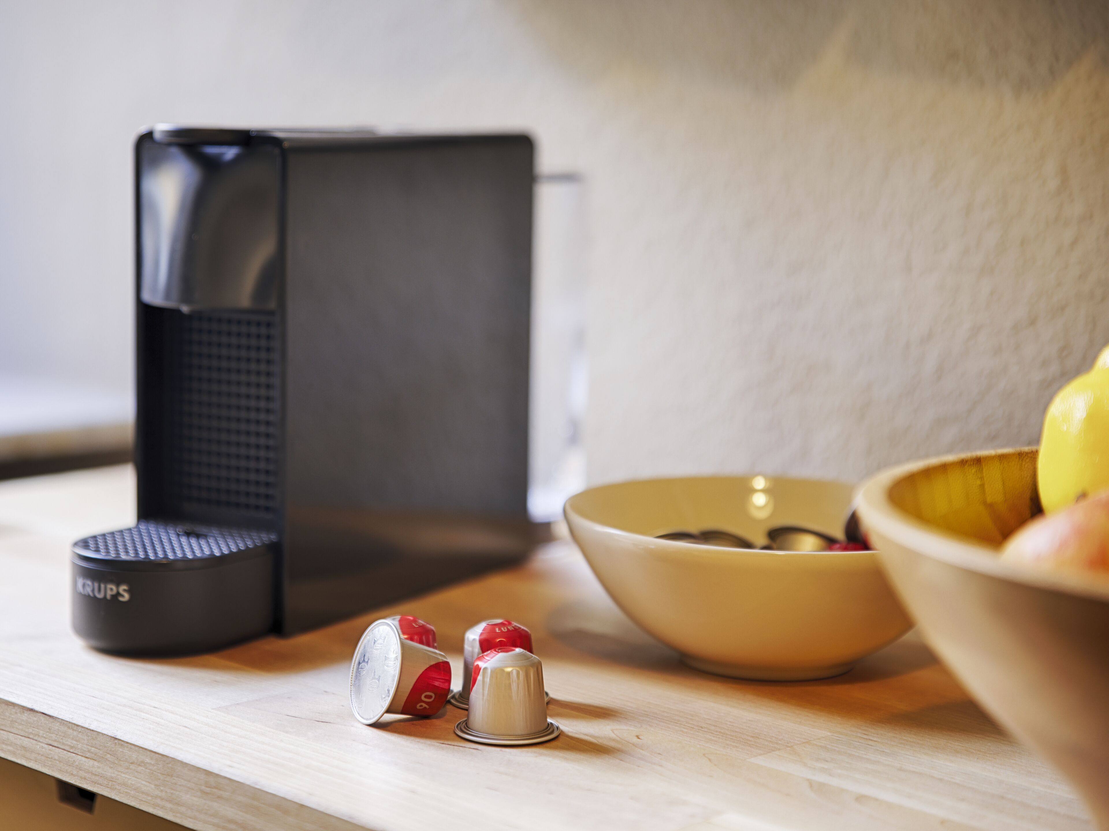 A kitchen counter with a coffee maker, a bowl of fruit, and a container labeled "KRUPS".