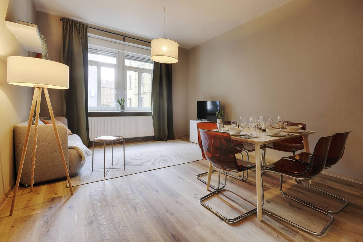 Un salon moderne avec un canapé, une table à manger dressée pour quatre personnes et un téléviseur.