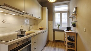 Pieni ja käytännöllinen keittiö, jossa on liesi, uuni ja pesuallas, ikkuna, josta on näkymä, sekä pieni puinen hylly, jossa on keittiötarvikkeita.