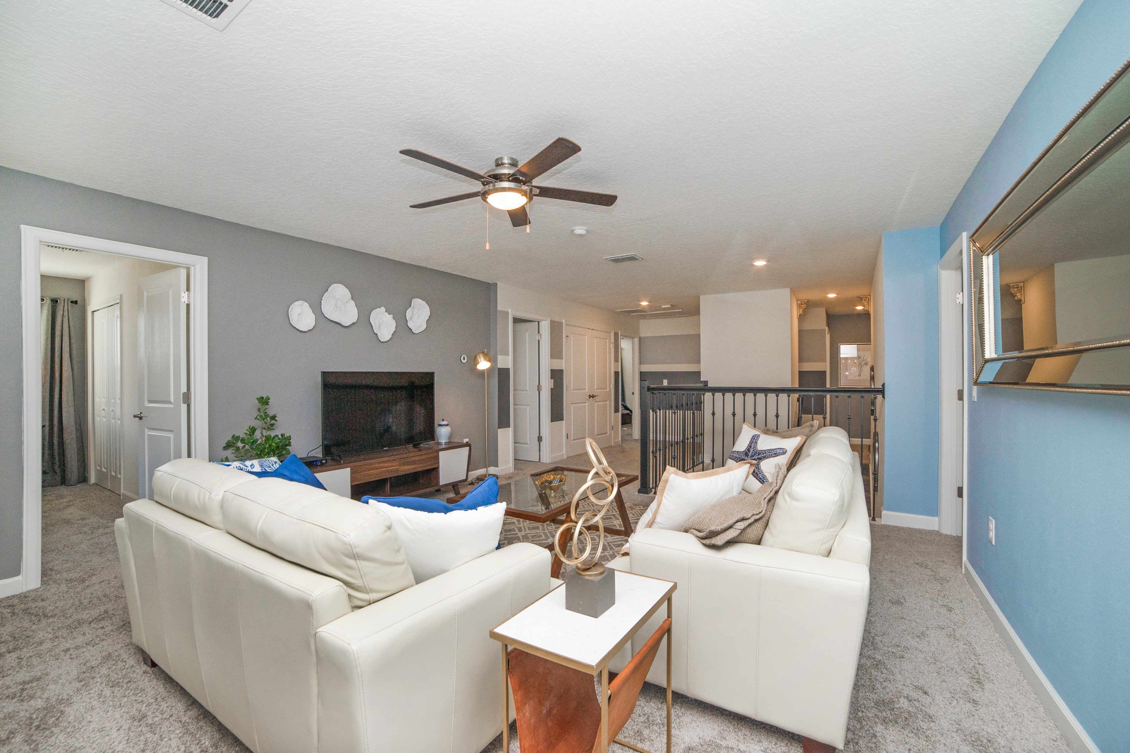 A modern living room with a ceiling fan, white sofas, a coffee table, and a TV.