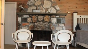 A stone fireplace with a sign reading "LAKE LIFE," two white chairs, and a bed with a headboard in a room with wooden walls. - Grand lake Cabin 3 @ Stony Point (Jay)