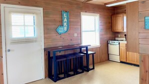 A small kitchen with wooden walls, a white door, a stove, and a sign indicating the direction to the lake. - Grand lake Cabin 3 @ Stony Point (Jay)