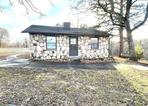 Un petit bâtiment en pierre, doté d’un toit sombre, d’une porte et de deux fenêtres.