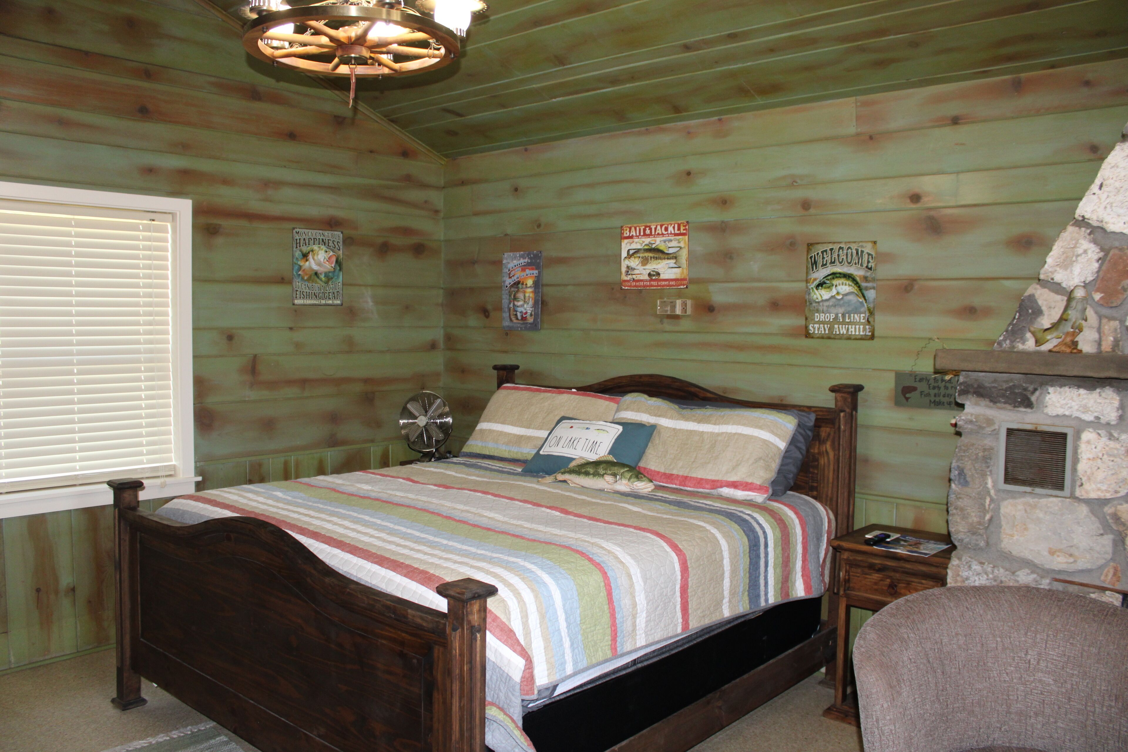 A wooden-paneled bedroom with a bed, a stone fireplace, and various wall decorations.