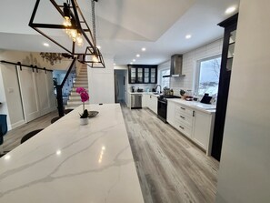 Una cocina moderna con una isla de mármol, electrodomésticos de acero inoxidable y una escalera que sube a otro nivel.