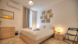 A neatly arranged bedroom with a bed, bedside tables, a chair, a dresser, and a wall with framed pictures. - Bright and modern apartment near seafront BFRA1-2 (Gzira)